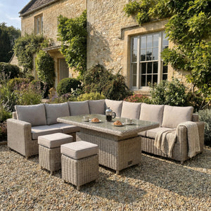 Amalfi large outdoor corner sofa set with riser table and two stools in a garden setting with a brick house