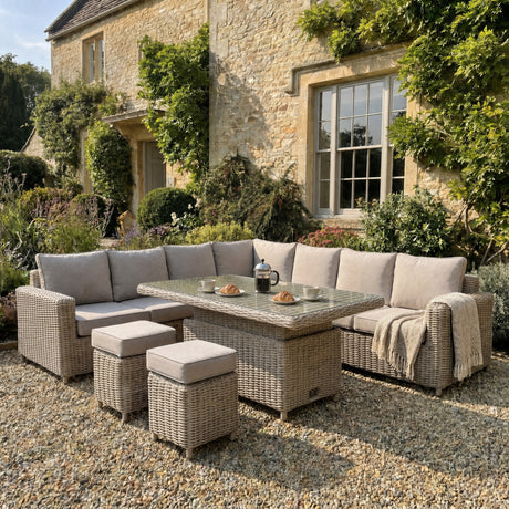 Amalfi large outdoor corner sofa set with riser table and two stools in a garden setting with a brick house