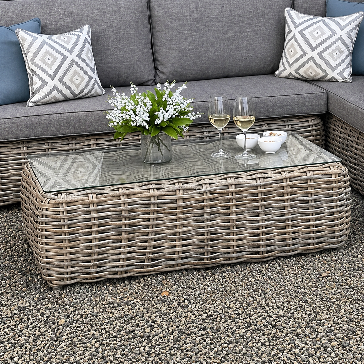 Outdoor patio setting with wicker coffee table, grey sofa, and decorative items.