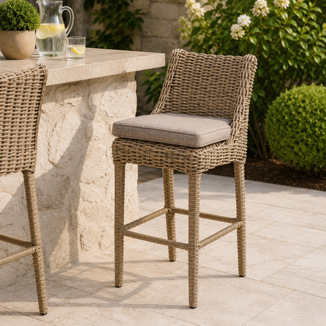 Wicker outdoor bar stools against a stone outside bar with a jug and glass of lemonade and flowers