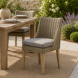 Wicker chair with a cushion in front of a wooden table outdoors.