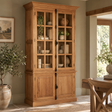 A tall rustic wooden display cabinet with glass-front upper doors and solid lower doors, styled in a warm, neutral-toned dining room.