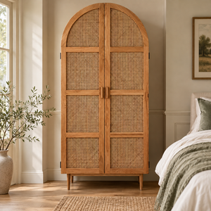 Arden arched oak wardrobe with woven rattan cane doors in a bright bedroom, beside a window and an olive tree