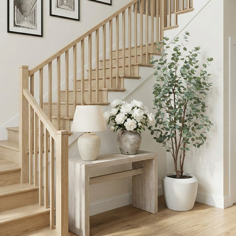 Staircase with wooden railings, a small table with a lamp and flowers, and a eucalyptus tree in a home interior.