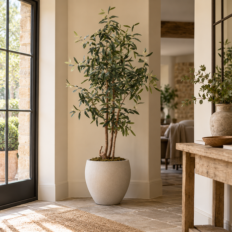 Artificial Olive Tree with Round White Planter in a stone-floored hallway, beside a glazed door and a rustic wooden console