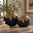 Two Aurum Round Black and Gold Vases in different sizes on a wooden sideboard, the larger holding olive branches, beside a stack of books