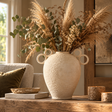 Avara Cotton Mache Large Vase With Decorative Handles filled with dried pampas and eucalyptus on a rustic wooden table beside a cream sofa