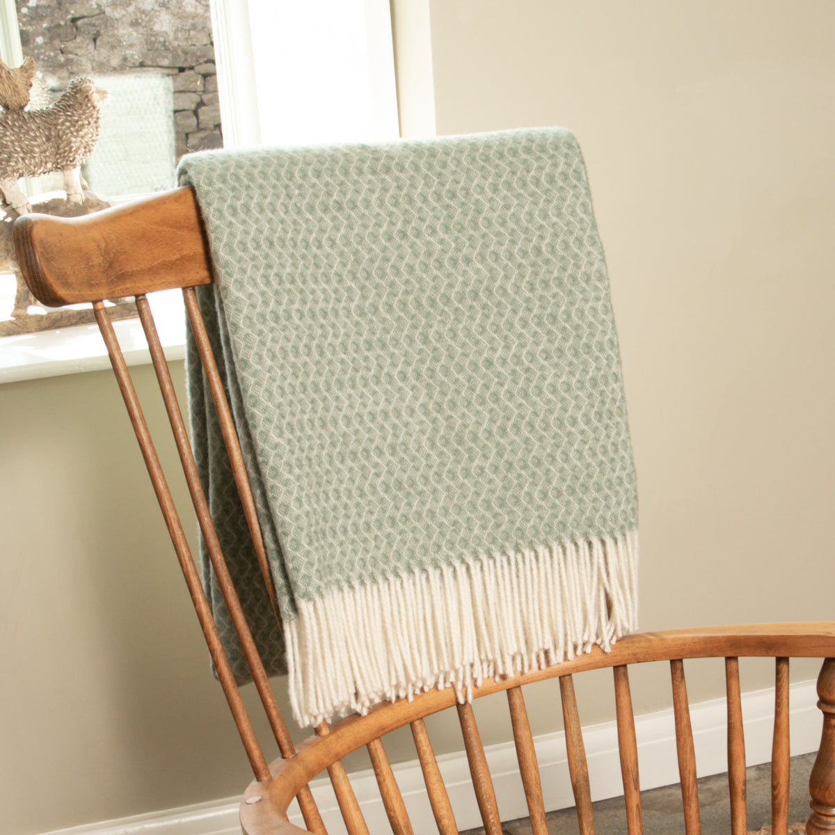 Hoop Pattern Green Wool Blanket hung over the back of a wooden Windsor chair, showing the tonal hoop weave and fringe
