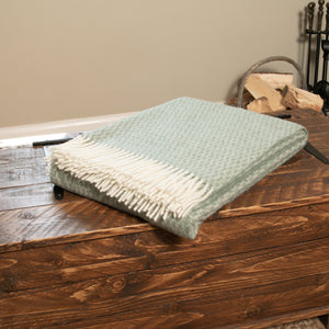 Hoop Pattern Green Wool Blanket folded on a wooden chest beside a log basket