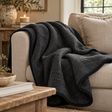 Black Merino Wool Blanket draped over a cream sofa with linen cushions, beside a rustic wooden table, a candle and a stoneware bowl