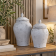 Two Bloomville Stone Ginger Jars in different sizes on a wooden console beside olive branches, a table lamp and a stack of books