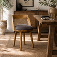 A wooden dining chair with a slatted back and a dark gray cushioned seat, placed in a warm, sunlit dining room next to a rustic wooden table.