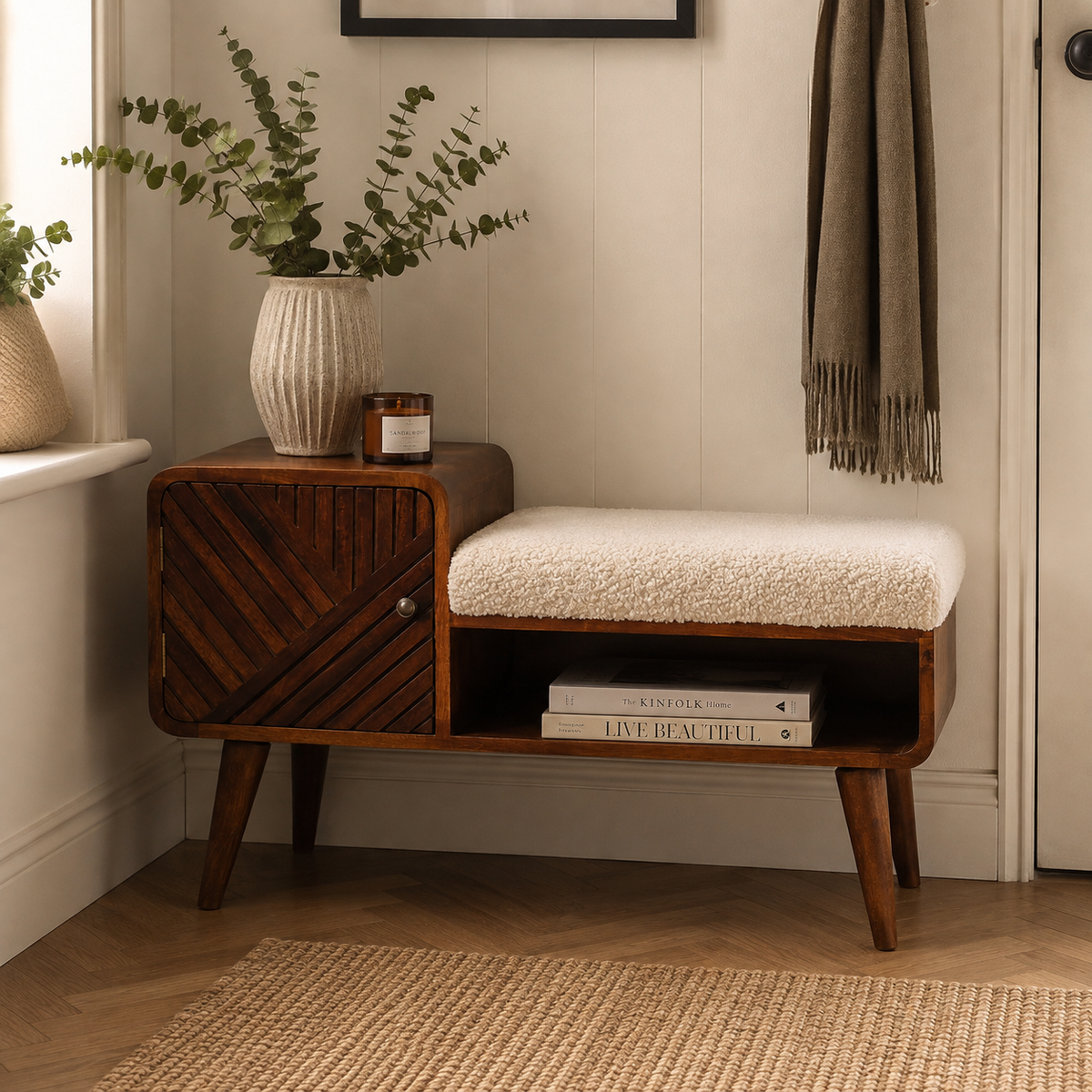 A mid-century modern wooden entryway bench with a cream bouclé seat cushion, shown in a styled home entryway next to a window with a potted eucalyptus and a hanging scarf.