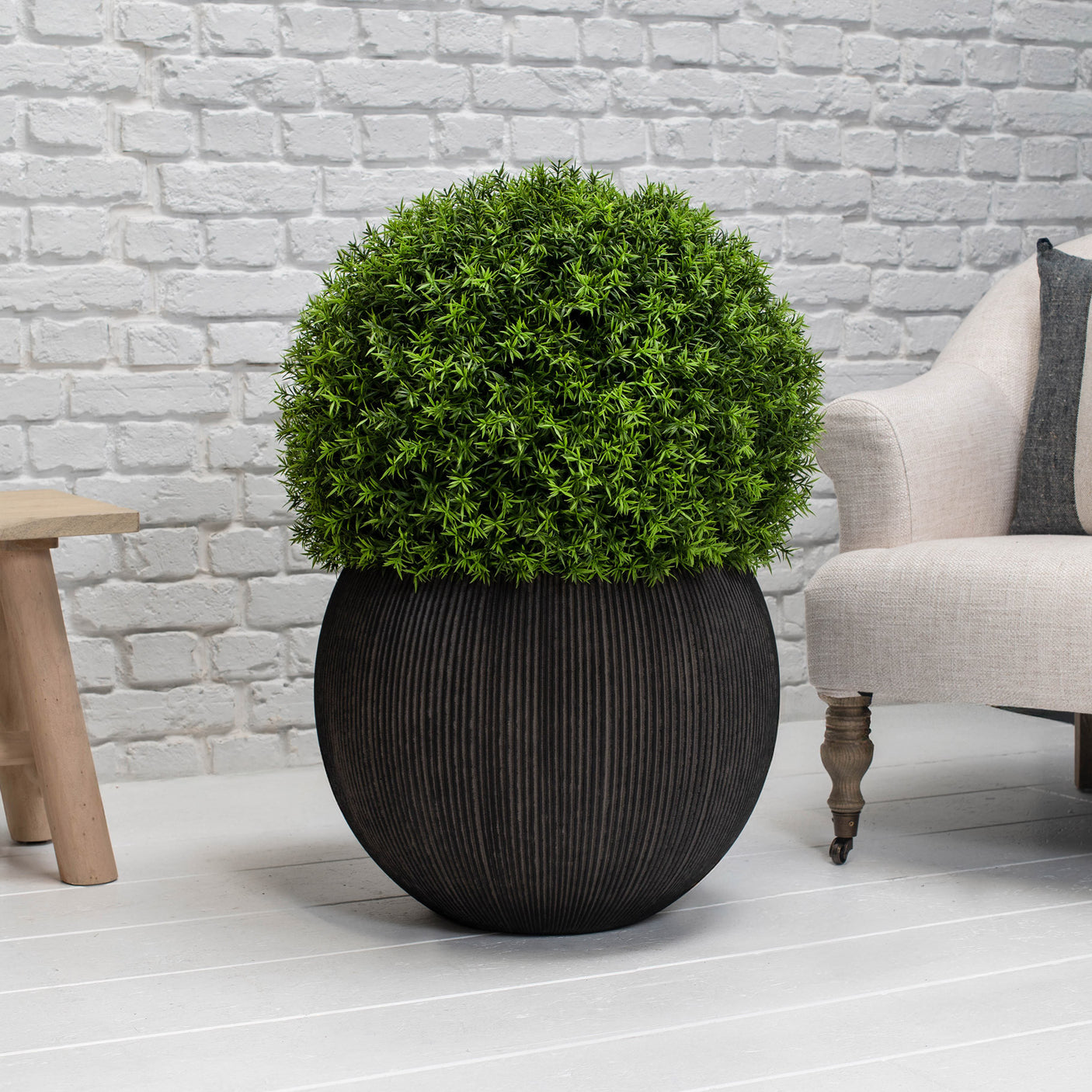 Brown planter with green bush on a white floor against a light grey brick wall.