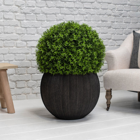Brown planter with green bush on a white floor against a light grey brick wall.