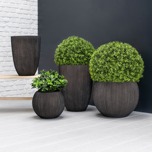 Set of dark brown planters with green plants against a white brick wall and black background