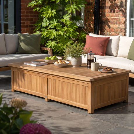A rectangular wooden outdoor coffee table with lift-up storage, styled on a patio with a sofa, greenery, and tableware in a real environment.