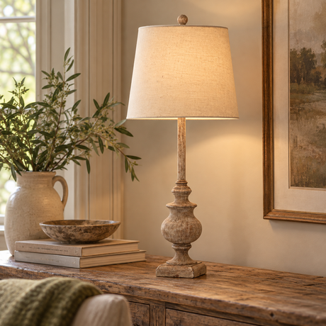 Chiaro Candlestick Table Lamp With Linen Shade lit on a rustic wooden console with olive branches in a stoneware jug