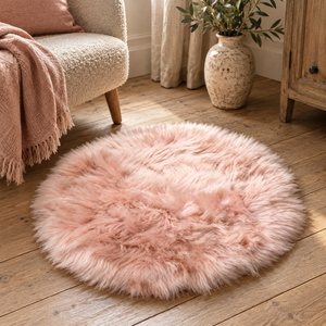Circular Pink Sheepskin Rug on a wooden floor beside a cream armchair with a pink throw