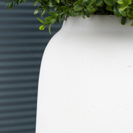 A close up of a textured off-white outdoor planter against a textured green background