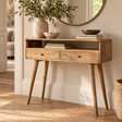 A mid-century modern wooden console table with two drawers and tapered legs, styled in a warm, sunlit room with home decor accessories.