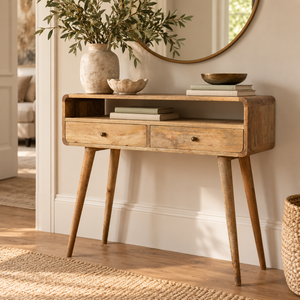 A mid-century modern wooden console table with two drawers and tapered legs, styled in a warm, sunlit room with home decor accessories.