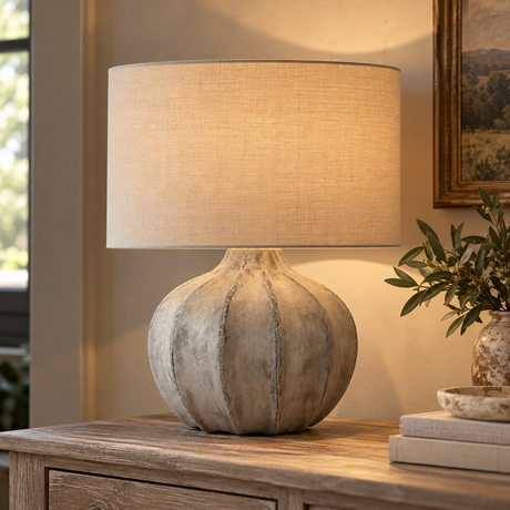 Darcy Antique White Flute Table Lamp lit on a wooden chest beside olive branches and books