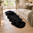 Double Black Sheepskin Rug on a wooden floor beside a cream sofa with green and patterned cushions