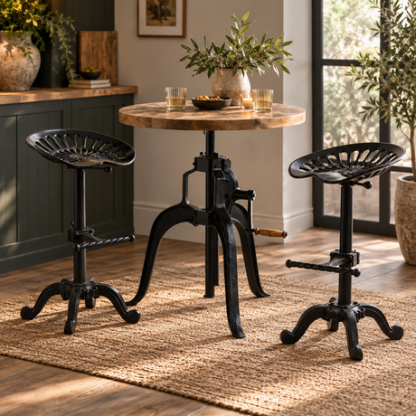 A rustic industrial bistro set featuring a round wooden table with a black metal height-adjustable pedestal base and two matching black bar stools with fan-shaped seats, shown in a warm, sunlit kitchen setting.