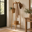 Envoy Oak Coat Stand beside a dark green front door, holding a scarf, felt hat and woven bag, with a lidded basket on its lower shelf