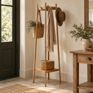Envoy Oak Coat Stand beside a dark green front door, holding a scarf, felt hat and woven bag, with a lidded basket on its lower shelf