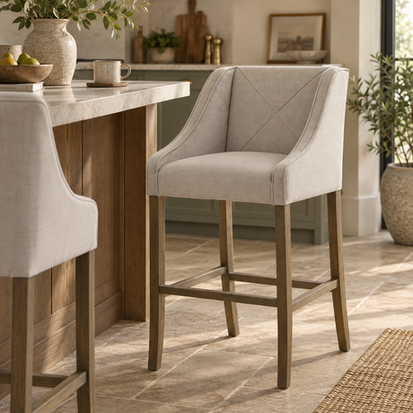 Light grey upholstered bar stool with curved arms and cross-stitched back, paired with a warm wood kitchen island in a neutral, modern rustic interior.