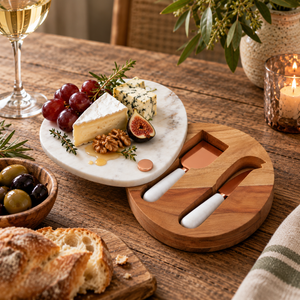 The Loxley Marble Cheese Board swivelled open with cheese, figs and grapes on top and two cheese knives stored in the wooden base, on a dining table.