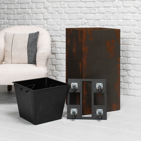 A black metal storage bin and matching black metal mounting brackets with casters, shown in front of a rusted brown metal cabinet in a living room setting with a white brick wall and a light-colored armchair.