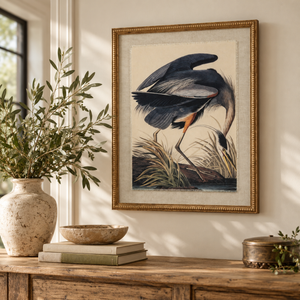 Flora & Fauna Heron print in a beaded oak-finish frame above a rustic wooden console table with olive branches in a stone vase, books and a wooden bowl