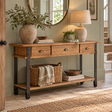 A rustic wood console table with black metal legs and casters, styled in a home entryway with a lamp, potted plant, and baskets.