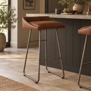 A single bar stool with a brown leather seat and twisted metal legs stands in a modern kitchen setting with a countertop, dark cabinets, and tiled floor.