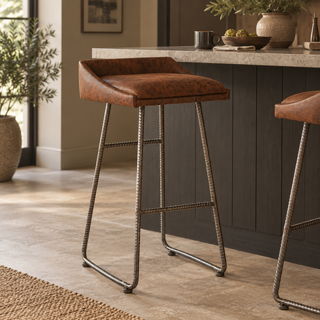 A single bar stool with a brown leather seat and twisted metal legs stands in a modern kitchen setting with a countertop, dark cabinets, and tiled floor.