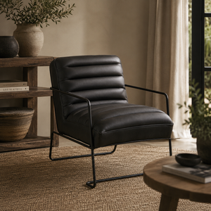 A modern black leather armchair with a ribbed backrest and slim black metal legs, styled in a warm, neutral-toned living room next to a wooden side table and window.