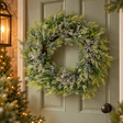 Frosted pine wreath with pinecones hanging on a sage green front door beside a lantern
