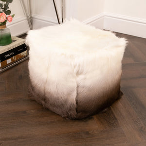 White goatskin pouffe on a wooden floor with books and a plant in the background