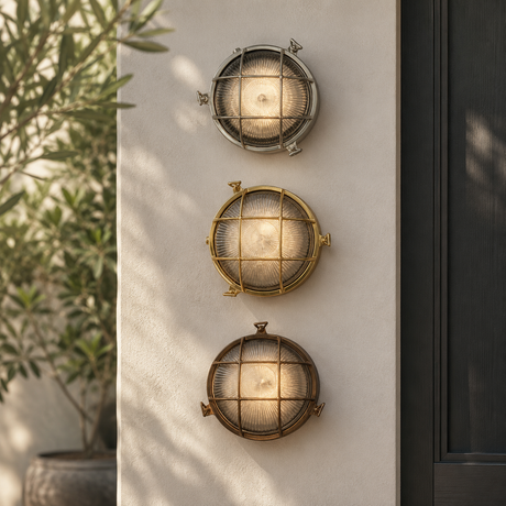 Three round outdoor wall sconces with ribbed glass shades and metal frames, mounted vertically on a beige stucco wall next to a dark door and greenery.