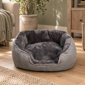 Grey Cord Plush Rectangle Snuggle Dog Bed with a textured grey outer and charcoal plush lining, on a wooden floor beside an armchair