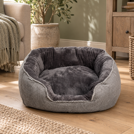 Grey Cord Plush Rectangle Snuggle Dog Bed with a textured grey outer and charcoal plush lining, on a wooden floor beside an armchair