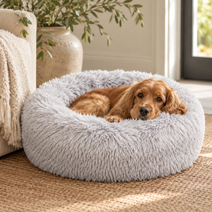Cocker spaniel curled up in the Grey Faux Fur Donut Dog Bed on a jute rug beside a cream armchair and a stoneware vase