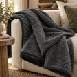 Grey Merino Wool Blanket in charcoal draped over a cream sofa with olive and linen cushions, beside a rustic wooden side table