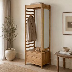 A tall light oak wood open wardrobe with a built-in mirror, two drawers at the bottom, and a coat hanging on a hanger. The coat rack is styled in a warm, minimalist room with a potted plant, a side table, and neutral-coloured walls.