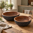 Two Hewn mango wood bowls with black dimpled exteriors on a rustic kitchen table