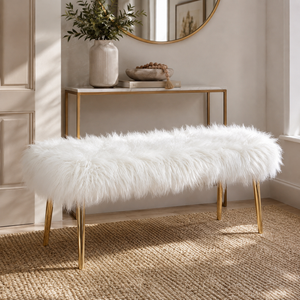 A white faux fur bench with slim gold metal legs, styled in a bright entryway next to a console table.