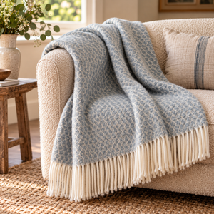 Hoop Pattern Blue Wool Blanket with a cream fringe draped over a cream boucle sofa beside a rustic wooden side table, jute rug and a vase of greenery